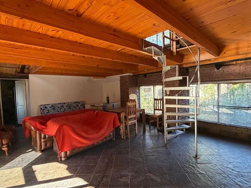 Spacious living area featuring exposed timber ceiling beams, a central spiral staircase, tiled flooring, and an exposed brick feature wall.