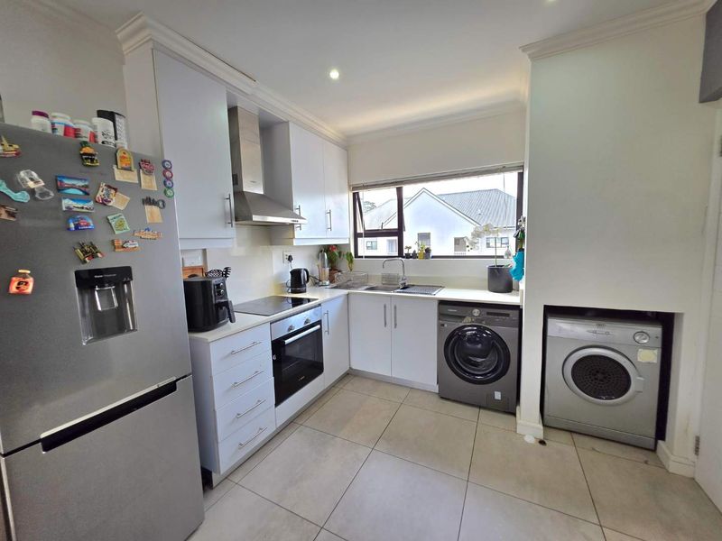 Modern kitchen featuring white cabinetry, integrated appliances, tiled flooring, and a functional layout with a dedicated space for laundry equipment.