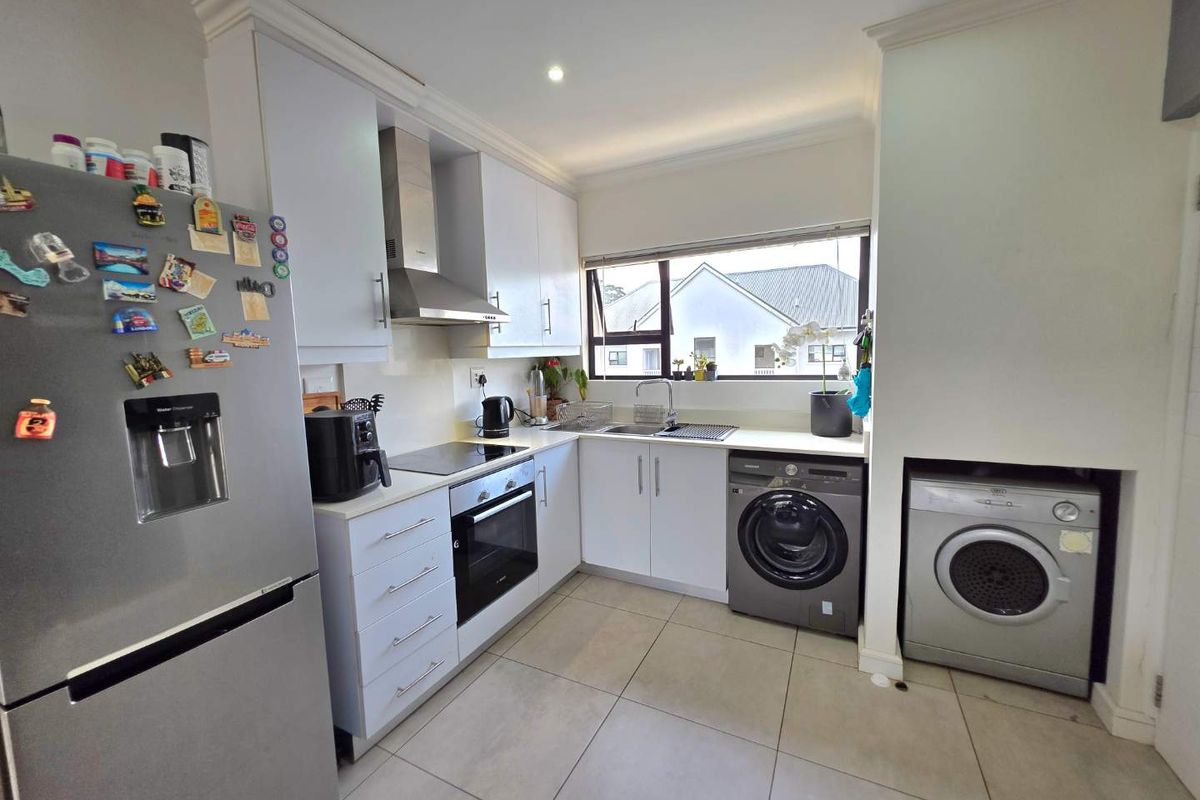 Modern kitchen featuring white cabinetry, integrated appliances, tiled flooring, and a functional layout with a dedicated space for laundry equipment.
