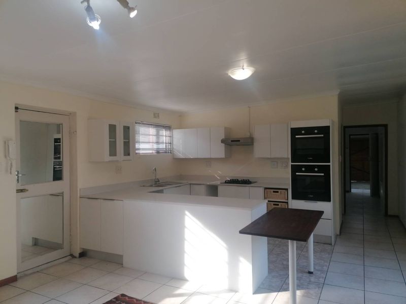 A functional kitchen featuring white cabinetry, a double wall oven, gas hob, extractor fan, and a breakfast counter with tiled flooring.