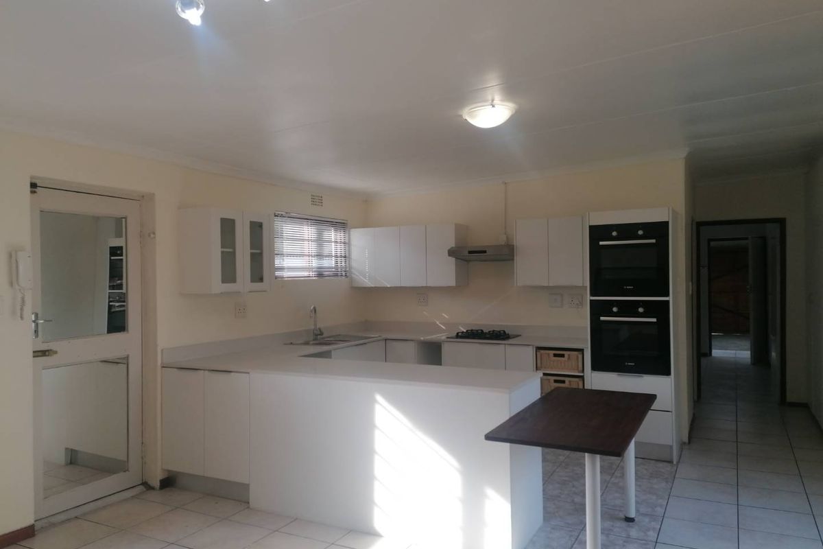 A functional kitchen featuring white cabinetry, a double wall oven, gas hob, extractor fan, and a breakfast counter with tiled flooring.
