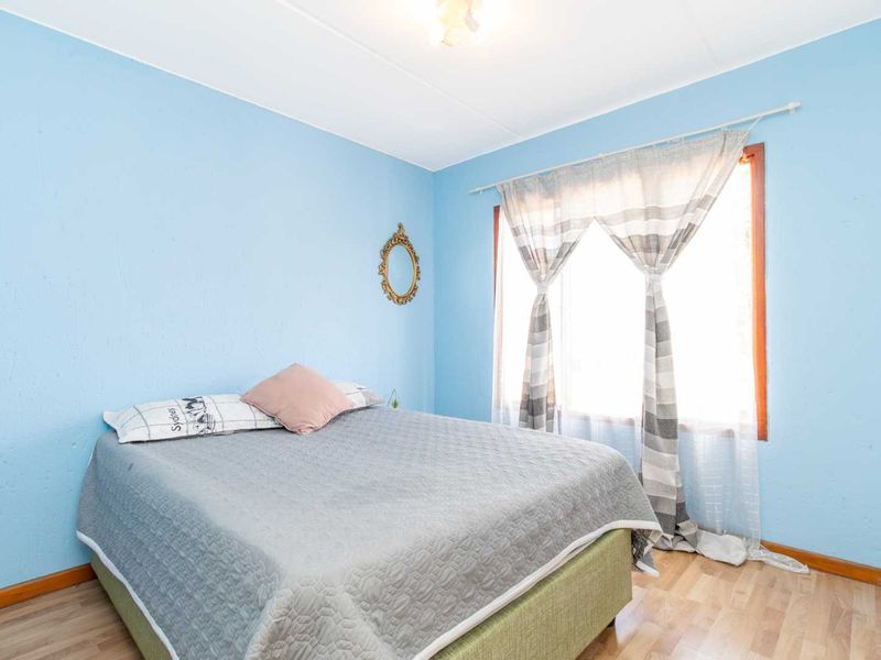 A bedroom featuring light blue walls, laminate flooring, and a window with timber framing.