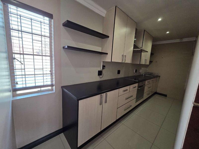 A clean, modern kitchen featuring light wood-tone cabinetry, dark countertops, integrated appliances, and tiled flooring, offering a functional and well-maintained workspace.