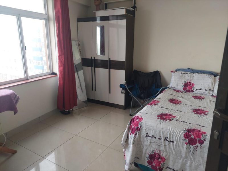 A functional bedroom featuring tiled flooring and a large window, providing natural light and a view of the surrounding area.