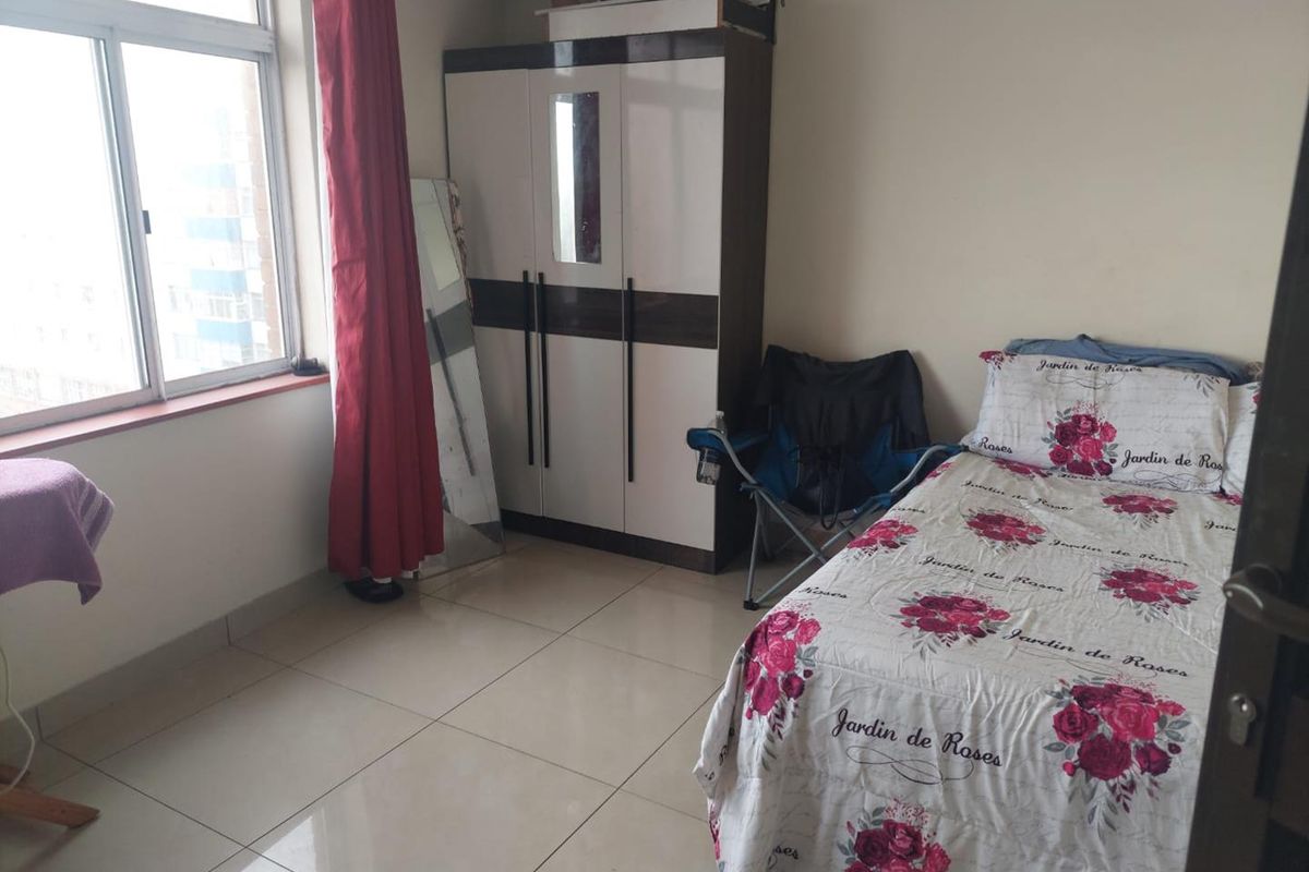 A functional bedroom featuring tiled flooring and a large window, providing natural light and a view of the surrounding area.