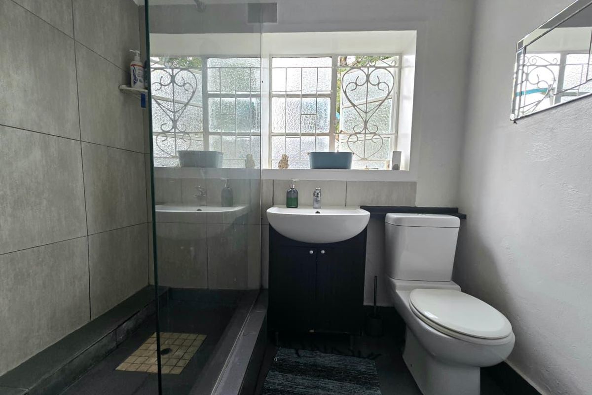 A functional bathroom featuring a glass-enclosed shower, a modern vanity basin, and a standard toilet, complemented by neutral wall tiling.