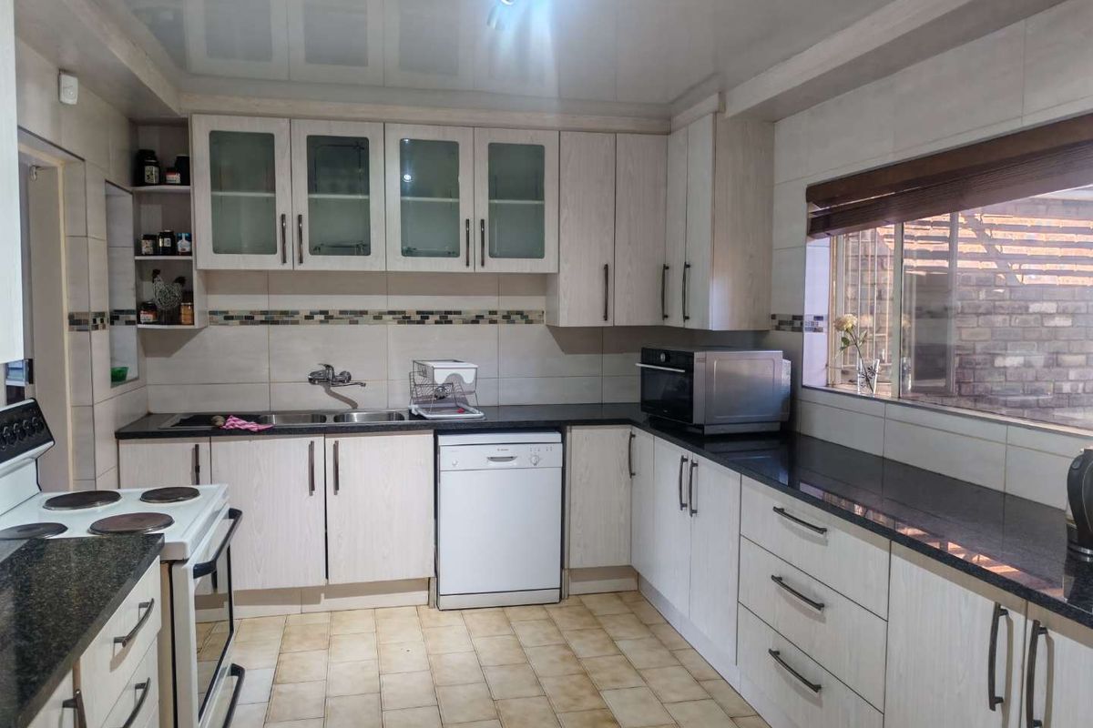 A functional kitchen featuring light wood-grain cabinetry, dark granite countertops, tiled backsplash, and integrated appliances with tiled flooring.