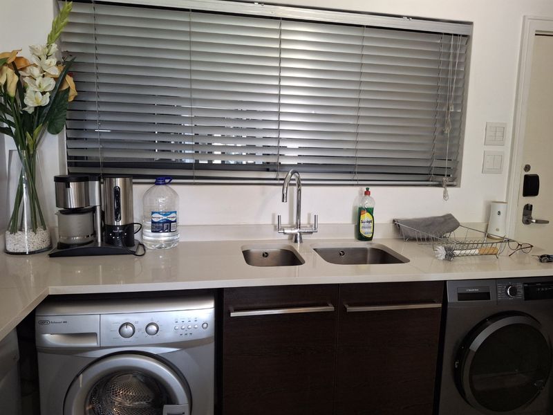 A functional laundry area featuring a stone countertop, double stainless steel sink, dark wood cabinetry, and integrated laundry appliances.