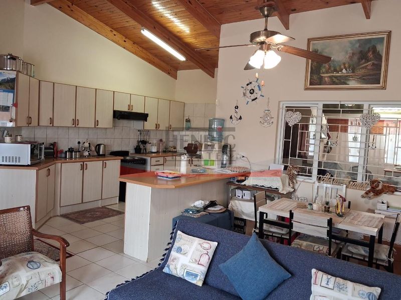 Open-plan kitchen and living area featuring exposed timber rafter ceilings, tiled flooring, and a breakfast bar, offering a functional layout with dated finishes.