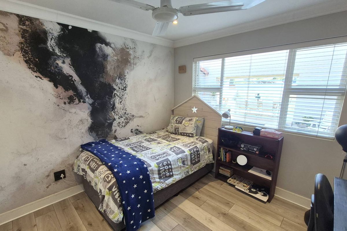 A well-maintained bedroom featuring wood-look tile flooring, a ceiling fan, and a decorative feature wall.