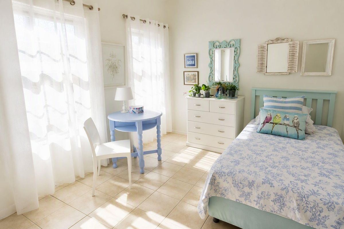 A bright and airy bedroom featuring neutral tiled flooring and large windows with natural light.
