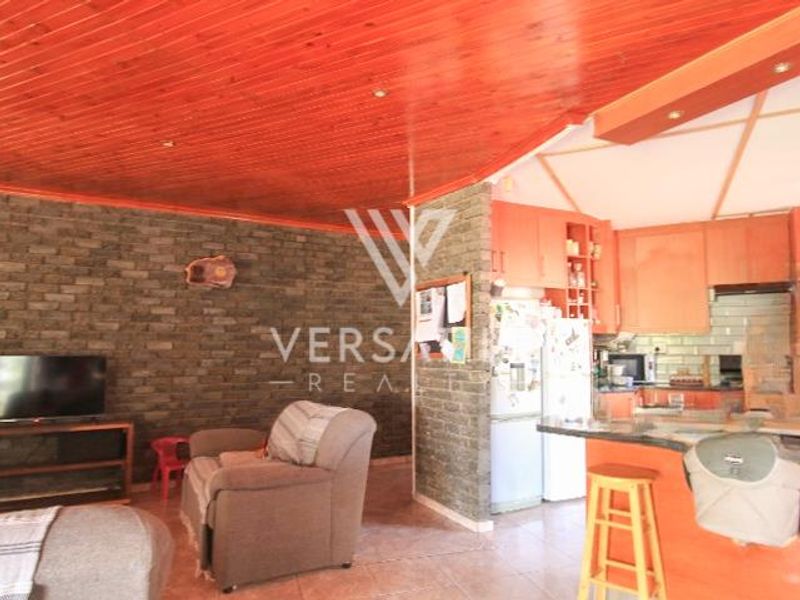 Open plan living and kitchen area featuring a stone clad feature wall, timber ceiling, and breakfast bar with integrated cabinetry.