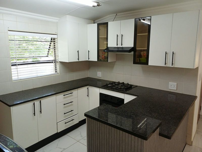 A modern kitchen featuring white cabinetry, dark granite countertops, a built-in gas hob, oven, and extractor fan with tiled flooring and backsplash.