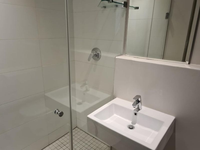 A clean, modern bathroom featuring a glass-enclosed shower, wall-mounted basin with chrome fixtures, and a large wall mirror.