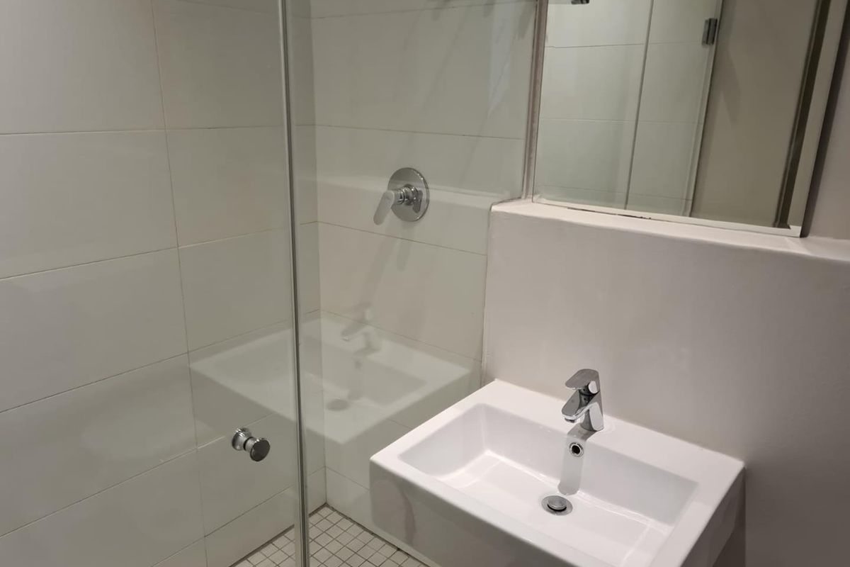 A clean, modern bathroom featuring a glass-enclosed shower, wall-mounted basin with chrome fixtures, and a large wall mirror.