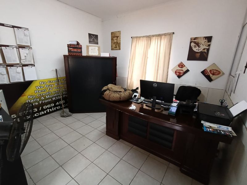 A functional office space featuring tiled flooring and a window with curtains, currently utilized as a workspace.