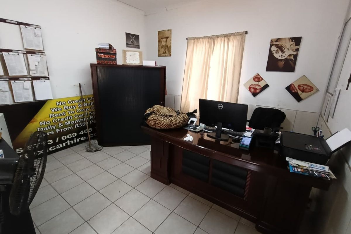 A functional office space featuring tiled flooring and a window with curtains, currently utilized as a workspace.