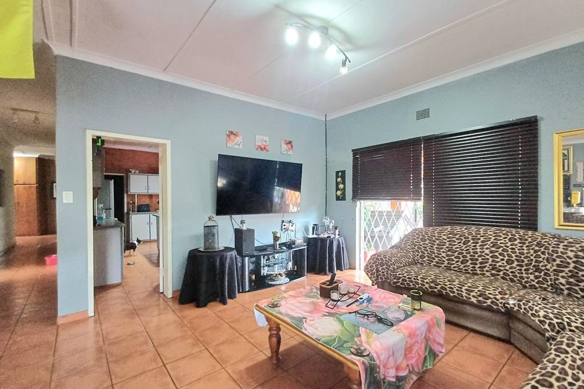 A spacious living room featuring tiled flooring, recessed ceiling lighting, and direct access to an adjacent kitchen area.