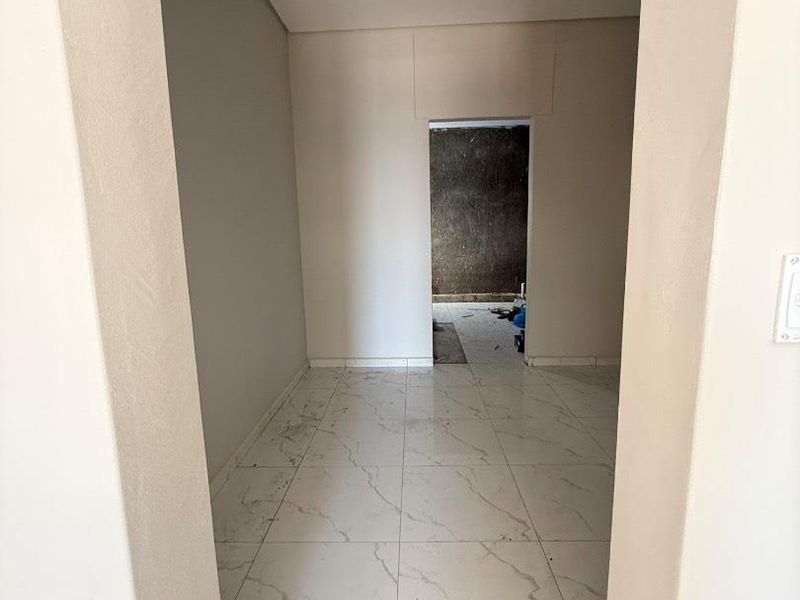 A vacant hallway featuring light-colored marble-look porcelain floor tiles and neutral wall finishes, currently in the final stages of construction.