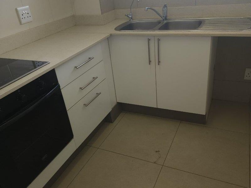 A functional kitchen featuring built-in cabinetry, an integrated oven and hob, double sink, and tiled flooring.