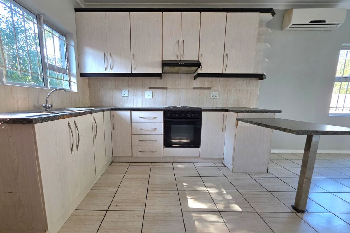 A functional kitchen featuring light wood-grain cabinetry, granite-look countertops, a built-in oven with extractor fan, and tiled flooring throughout.
