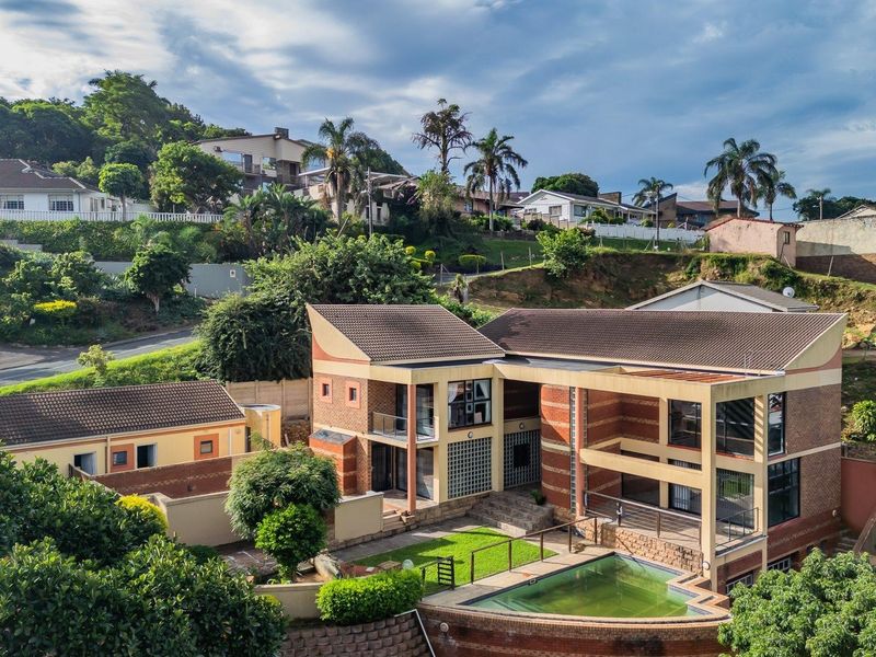 Aerial view of a multi-level residential property featuring a brick facade, tiled roof, private swimming pool, and landscaped garden area.