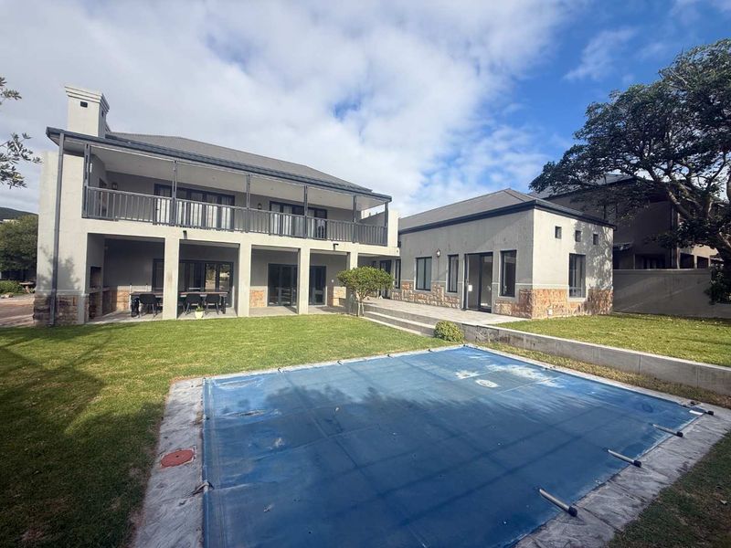 Rear view of a two-story house featuring a swimming pool with cover, a covered patio, a balcony, and stone-clad exterior detailing.