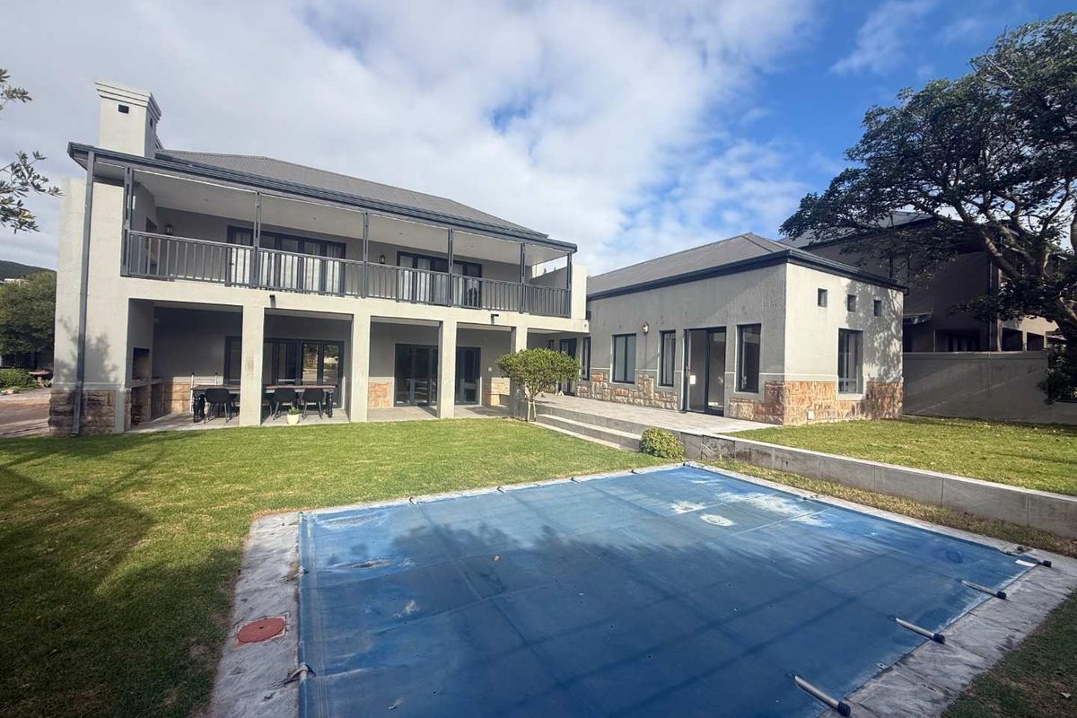 Rear view of a two-story house featuring a swimming pool with cover, a covered patio, a balcony, and stone-clad exterior detailing.