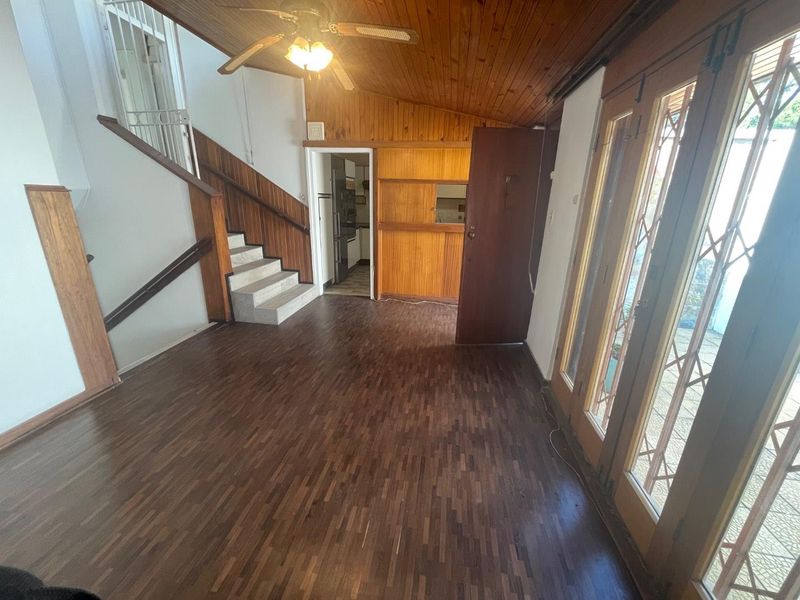 Spacious living area featuring parquet flooring, timber ceiling paneling, and direct access to the patio through timber-framed glass doors with security gates.