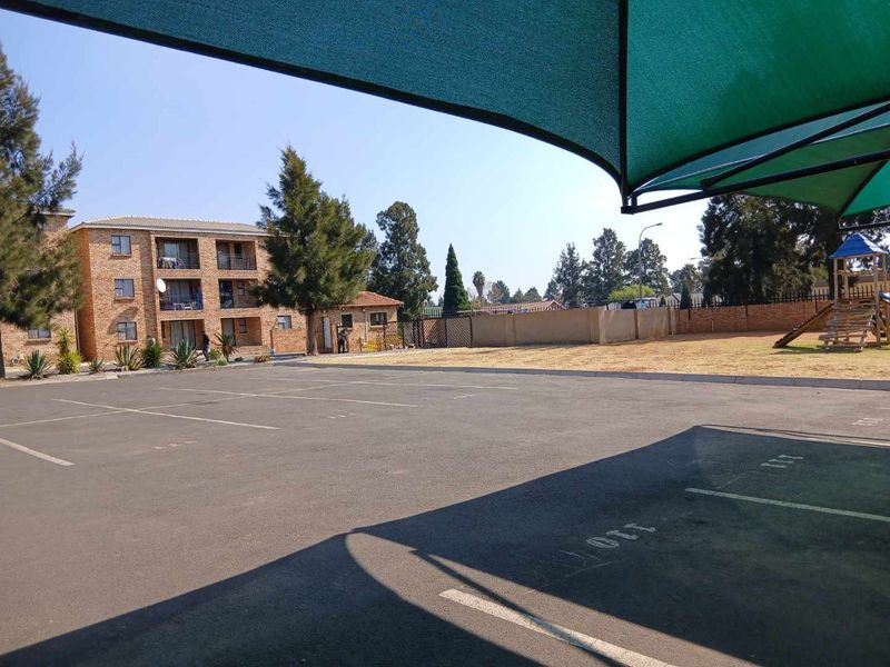 Exterior view of the townhouse complex featuring a paved parking area with shade cloth carports and a communal children's play area.
