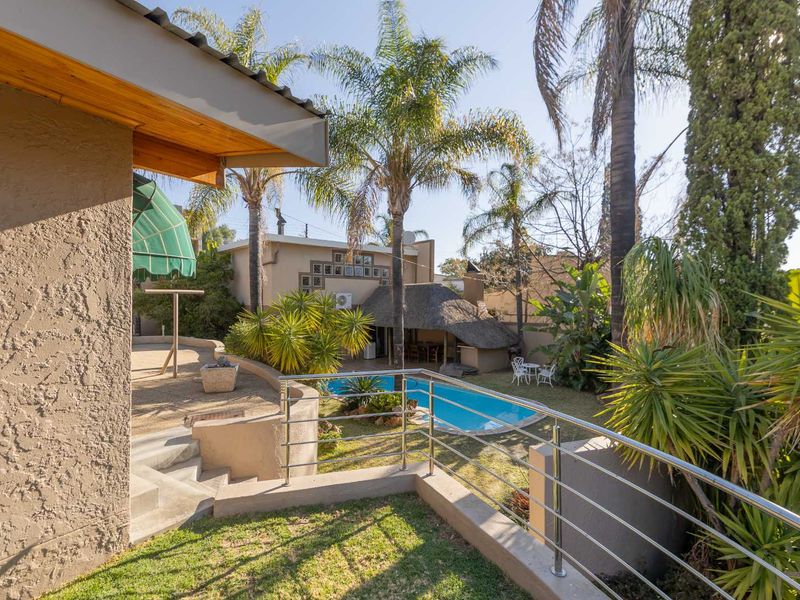 Rear garden view featuring a swimming pool, a thatched lapa entertainment area, and a raised terrace with stainless steel balustrades.