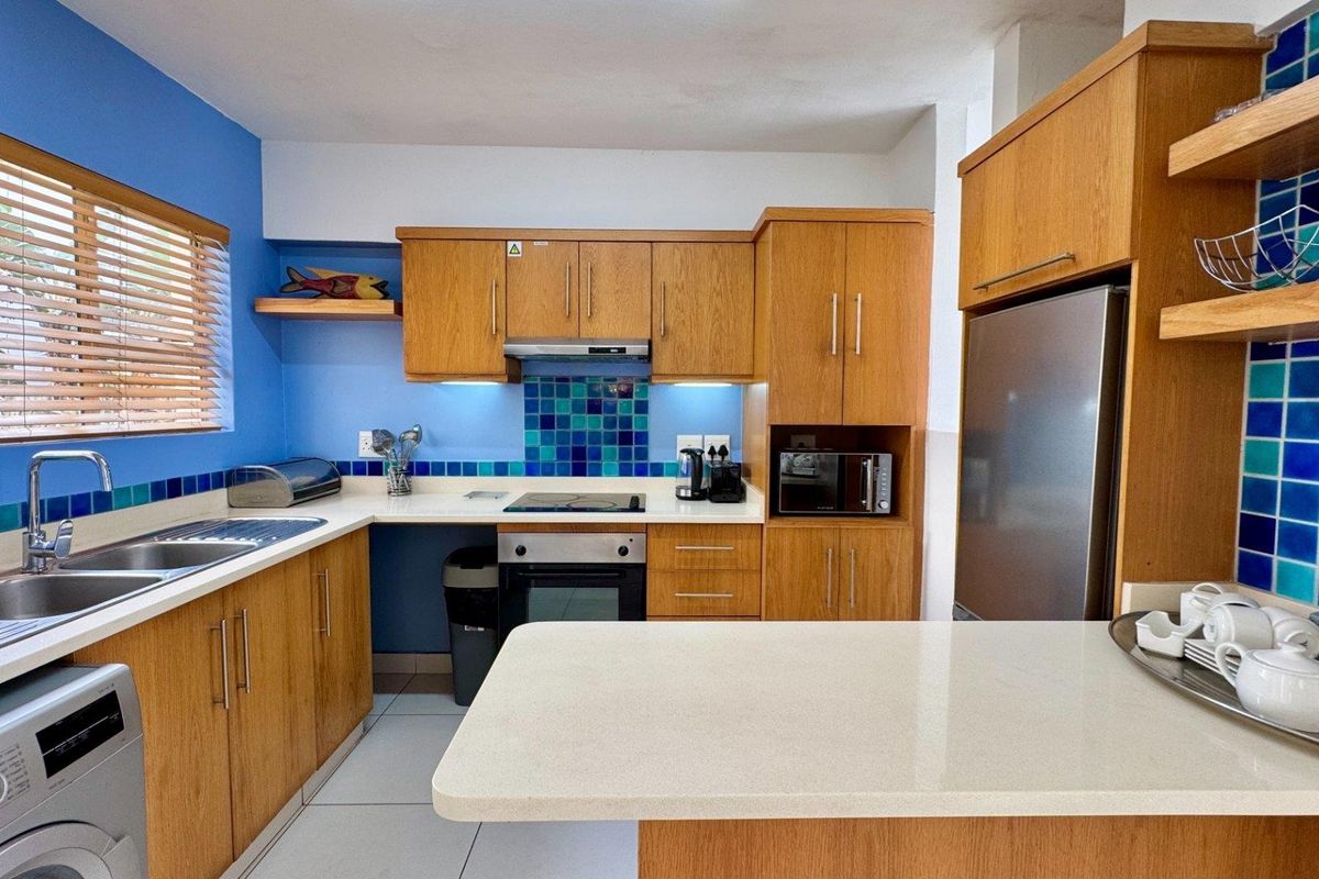 A functional kitchen featuring wooden cabinetry, stone countertops, a tiled splashback, and integrated appliances, offering a bright and practical workspace.