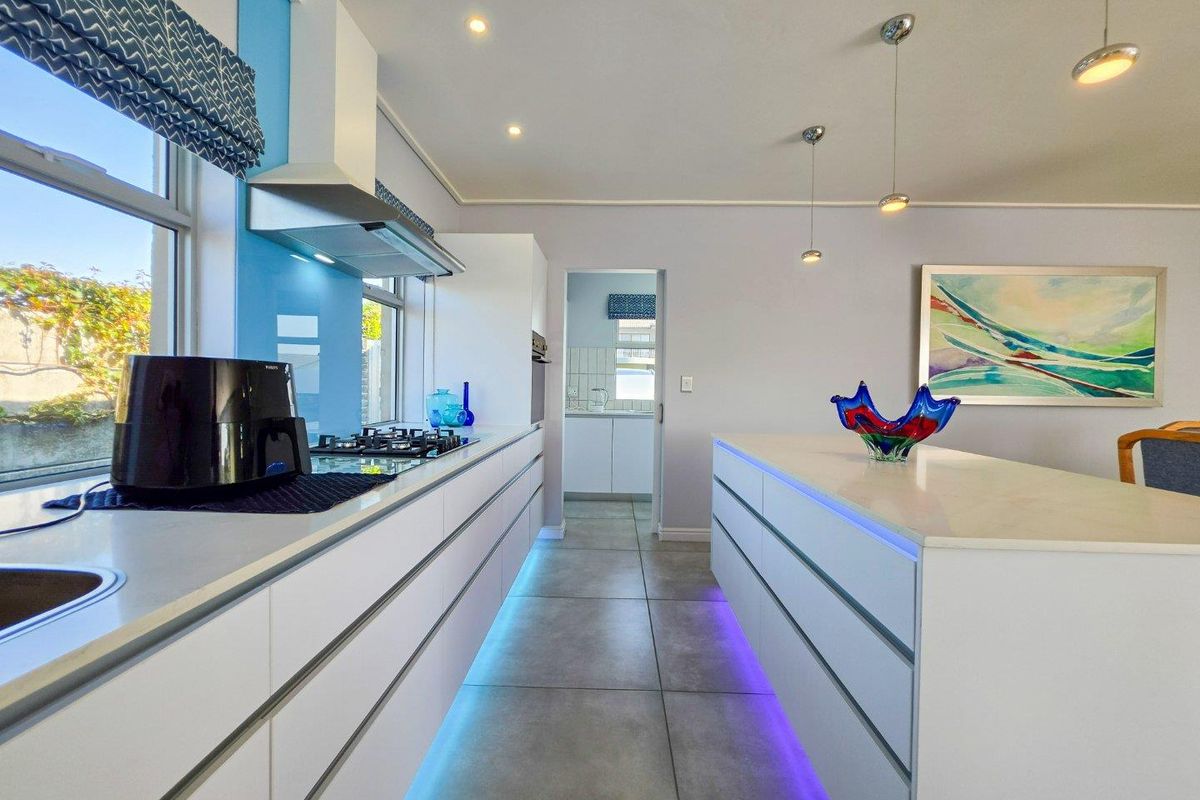Modern kitchen featuring a central island, stone countertops, gas hob, integrated extractor, and stylish under-cabinet LED lighting with a scullery access.