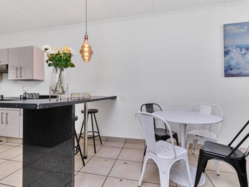 Open-plan kitchen and dining area featuring a granite breakfast bar, neutral cabinetry, and ceramic tiled flooring.