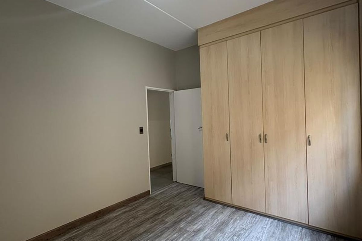 A clean, empty bedroom featuring modern wood-look laminate flooring and extensive built-in cupboard storage.