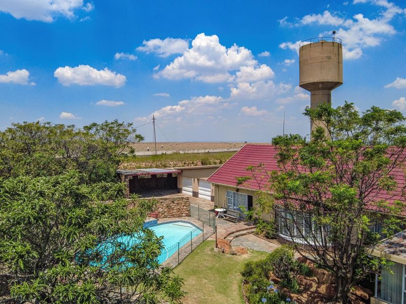 Aerial view of the property featuring a swimming pool, paved patio area, garage, and a prominent water tower set within a landscaped garden.