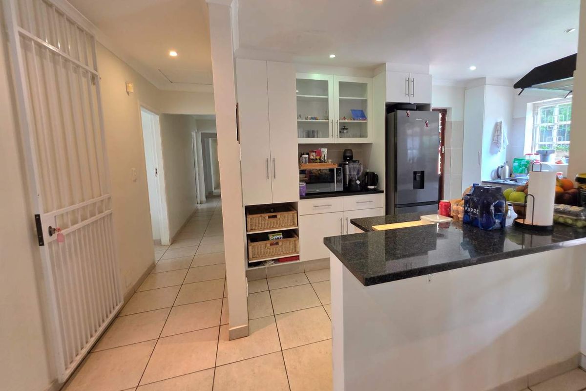 A functional kitchen featuring granite countertops, ample built-in cabinetry, and tiled flooring, seamlessly connected to the home's hallway and living areas.