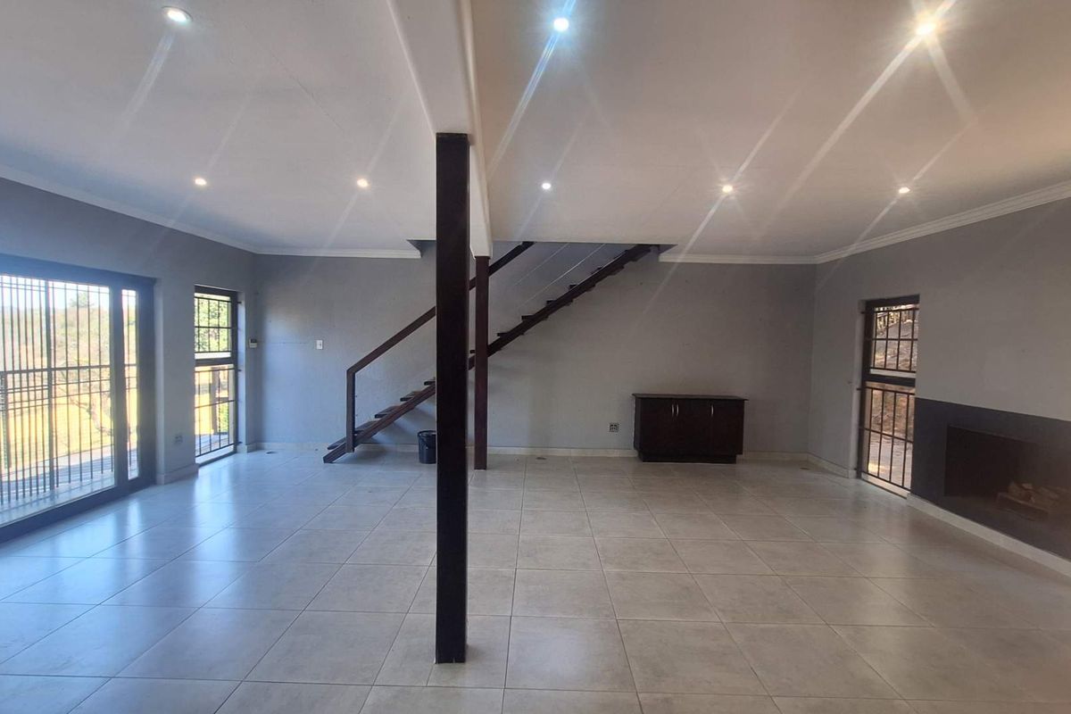 Spacious open-plan living area featuring neutral ceramic floor tiles, a built-in fireplace, modern recessed lighting, and a staircase leading to the upper level.