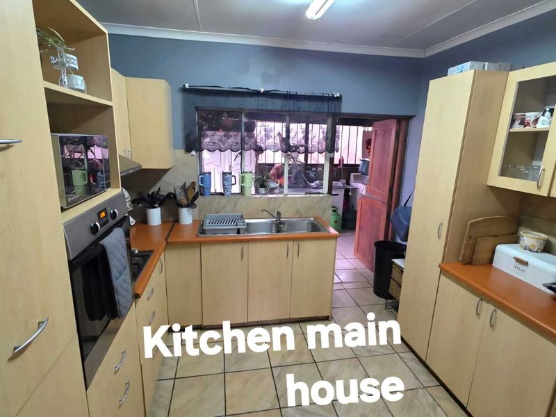 A functional kitchen featuring light wood-toned cabinetry, laminate countertops, a stainless steel double sink, and tiled flooring with a view into the adjacent utility area.