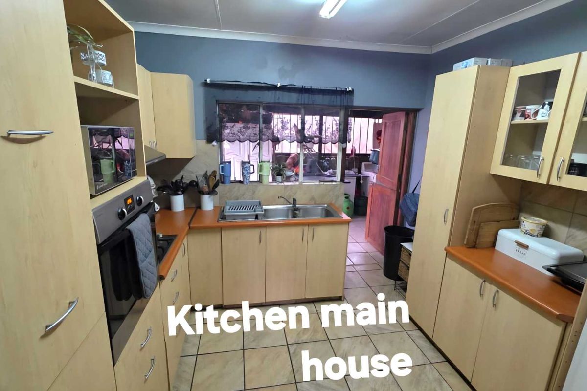 A functional kitchen featuring light wood-toned cabinetry, laminate countertops, a stainless steel double sink, and tiled flooring with a view into the adjacent utility area.