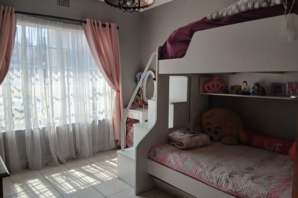 A bedroom featuring tiled flooring, a ceiling light fixture, and a ventilation grille, with natural light entering through a large window.