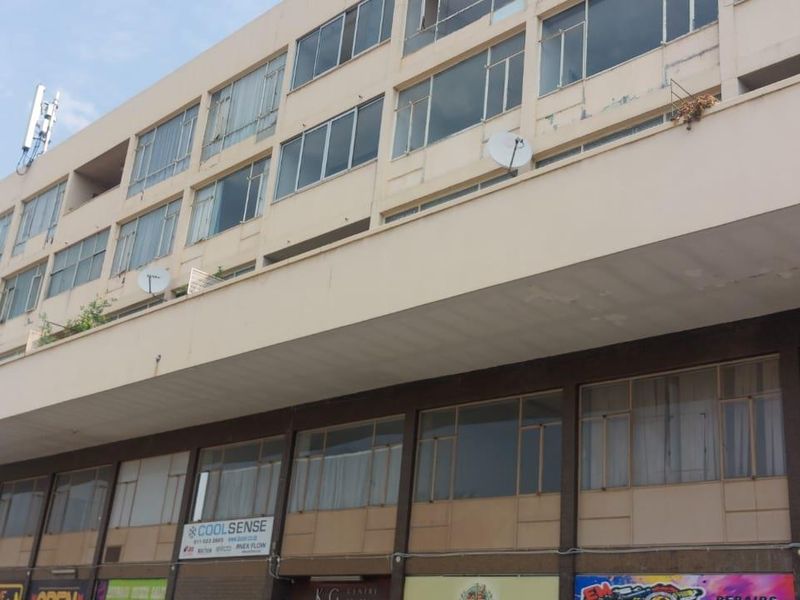 Exterior view of a multi-story townhouse complex featuring ground-floor commercial storefronts and upper-level residential units with balconies.