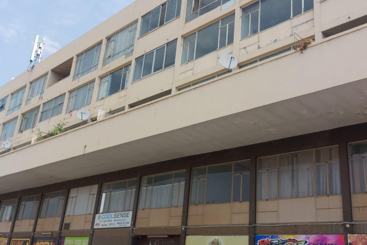 Exterior view of a multi-story townhouse complex featuring ground-floor commercial storefronts and upper-level residential units with balconies.