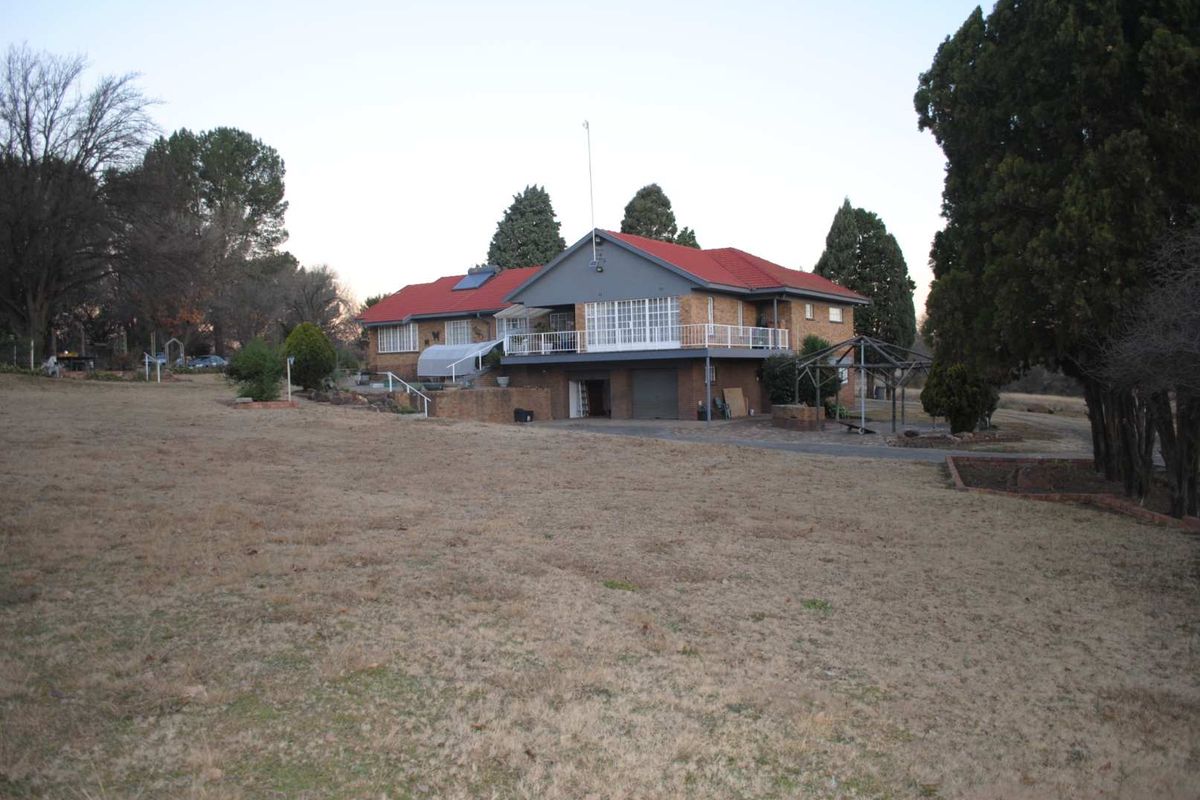 Rear view of a brick small holding property featuring a tiled roof, elevated balcony, and integrated garage set on a large plot.