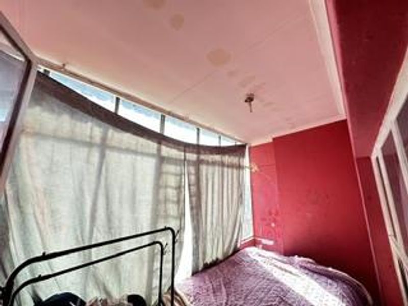 A bedroom featuring large windows and visible ceiling water damage, requiring maintenance and cosmetic updates to improve the overall condition.
