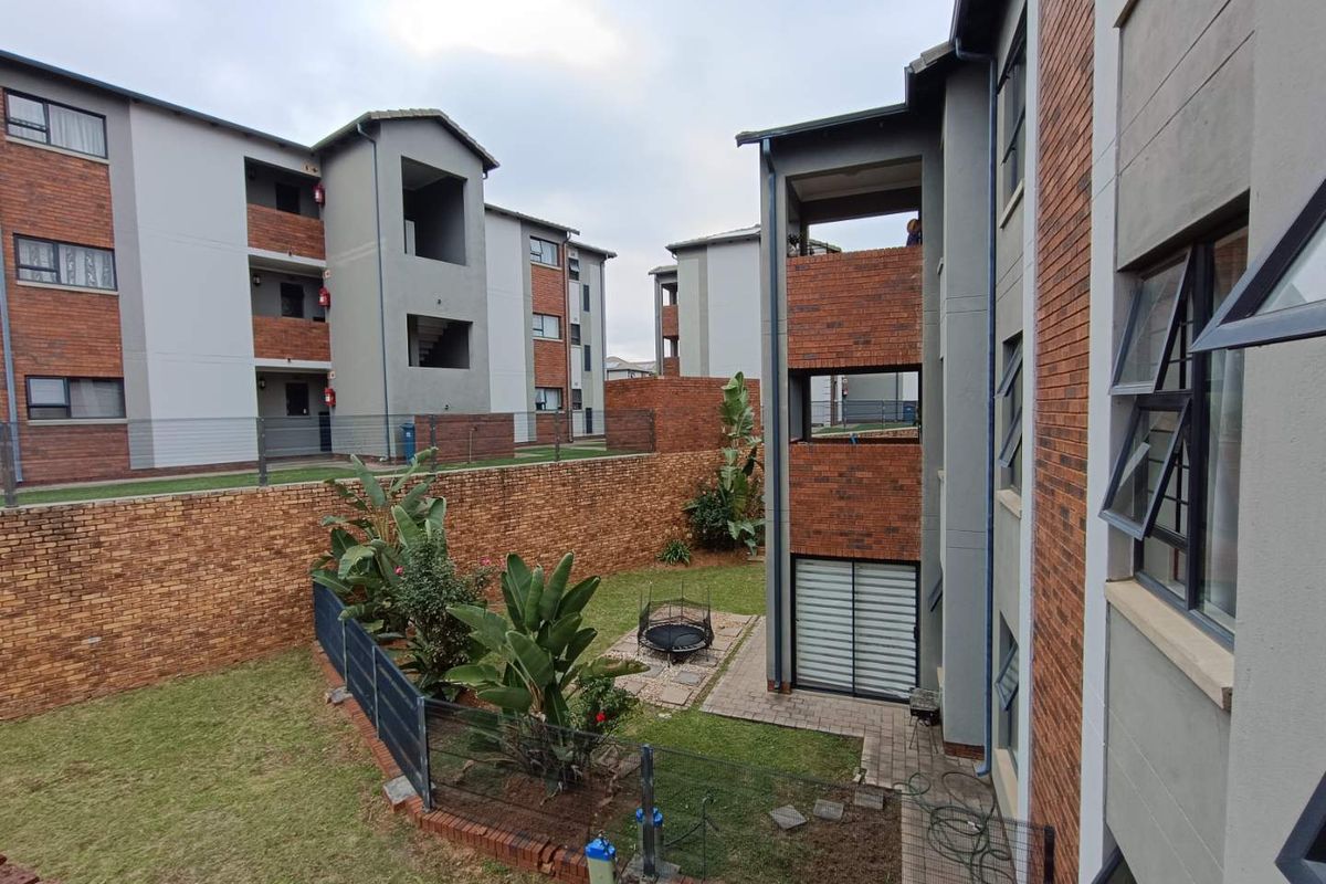 View of the apartment complex exterior, featuring brick and plaster facades, communal garden space, and private ground-floor patio areas.