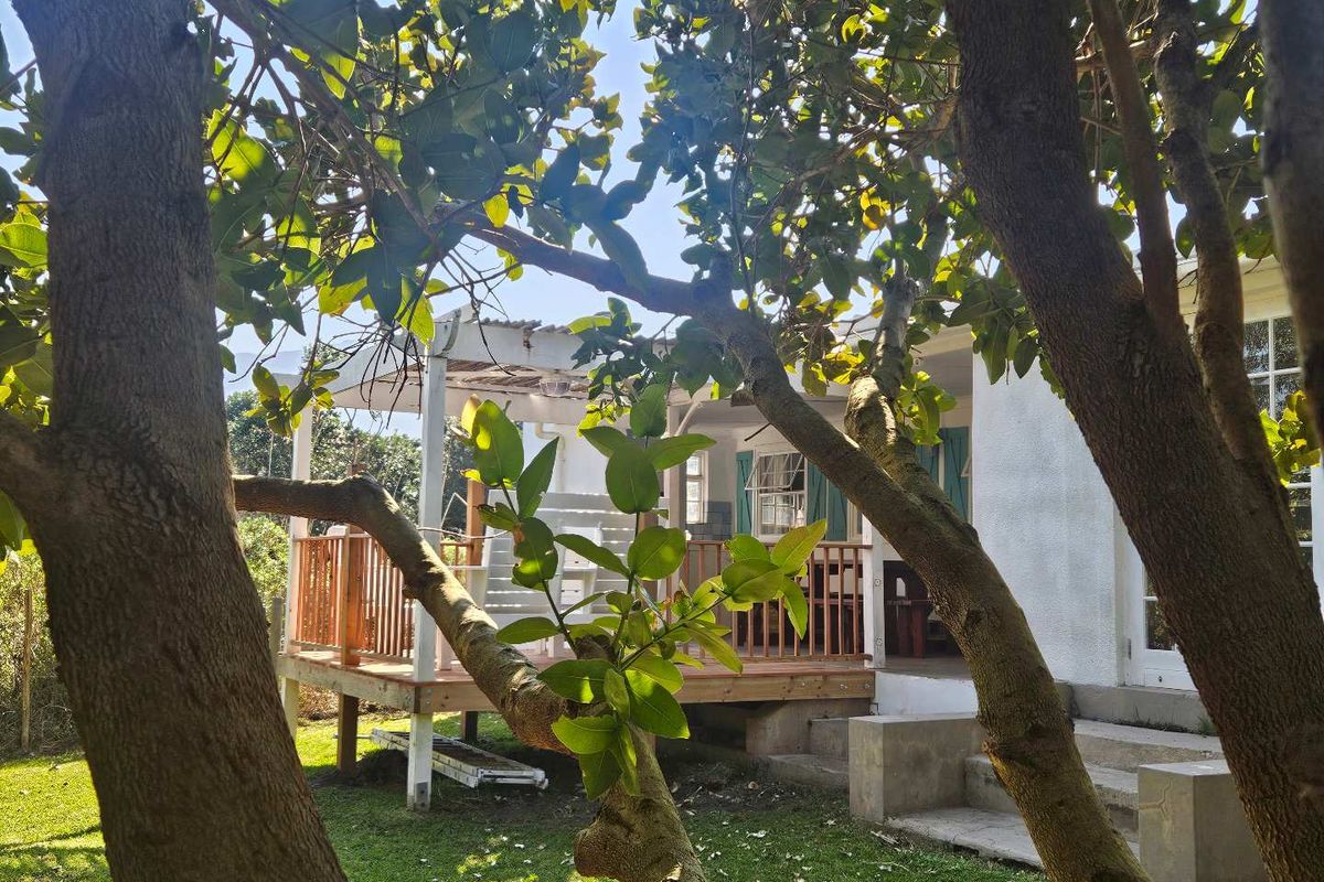 A view of the rear exterior featuring a raised wooden deck with a timber balustrade and concrete steps leading to the garden.