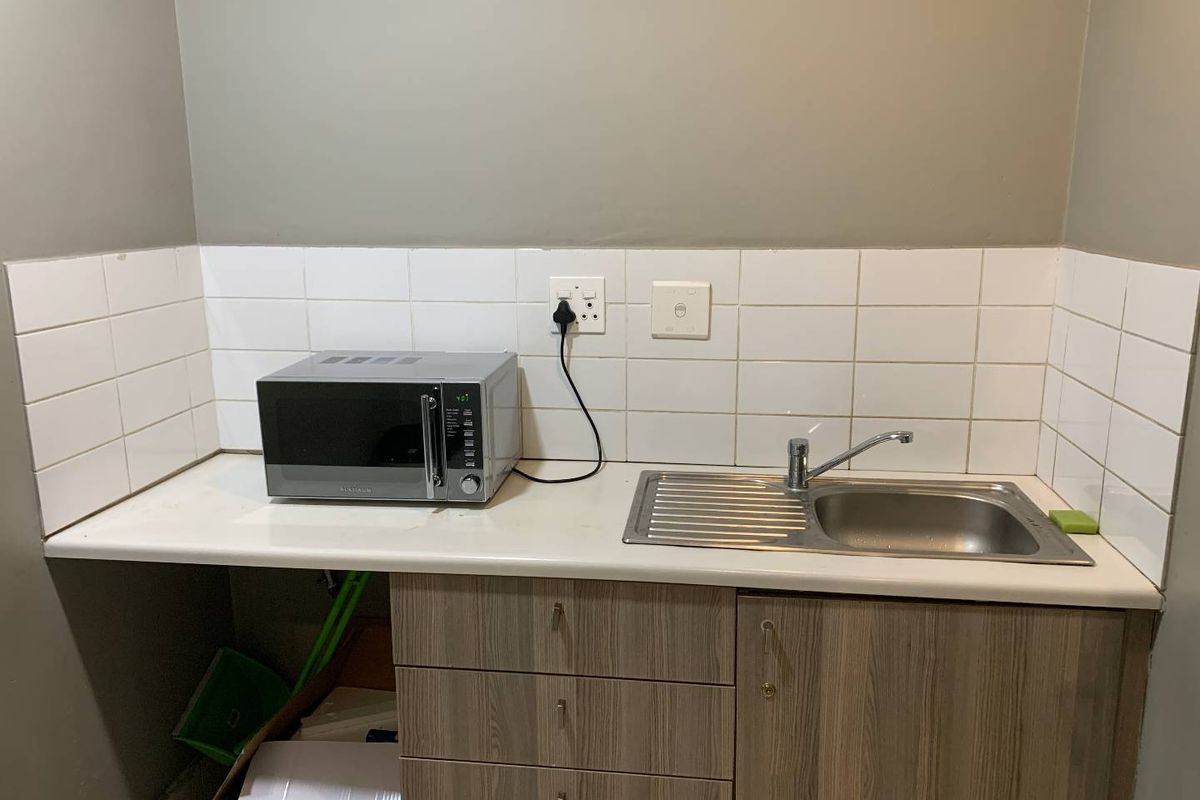 A compact kitchenette area featuring a stainless steel sink, tiled splashback, and built-in wooden cabinetry with a countertop.