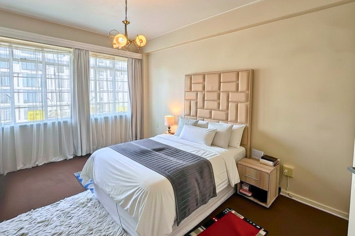 A well-lit bedroom featuring large windows, neutral wall finishes, and carpeted flooring, providing a comfortable and functional living space.
