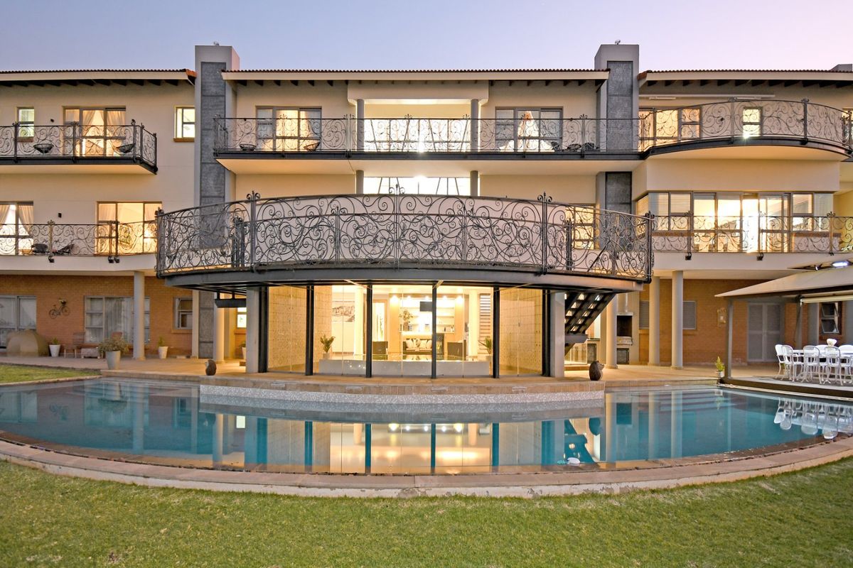 Rear elevation of a multi-story residence featuring a swimming pool, expansive wrought iron balconies, and a covered patio area with built-in braai facilities.
